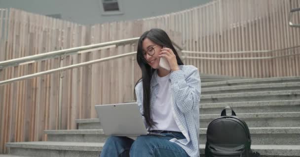 Улыбающиеся Азиатские Молодые Студентки Сидят Лестнице Помощью Ноутбука Разговаривают Мобильному — стоковое видео