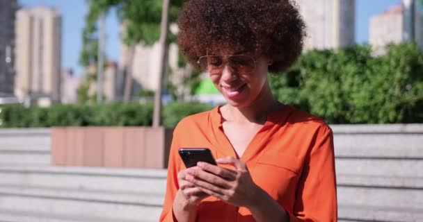Νεαρή Αφροαμερικανή Γυναίκα Σγουρά Μαλλιά Κρατώντας Smartphone Σερφάρισμα Χρησιμοποιώντας Εφαρμογές — Αρχείο Βίντεο