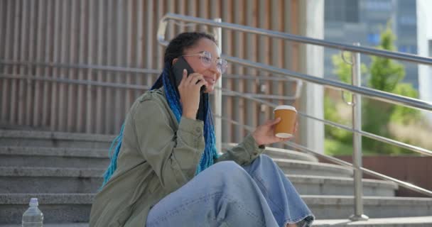 Młoda Afrykańska Studentka Rozmawia Przez Telefon Pije Kawę Siedząc Zewnątrz — Wideo stockowe