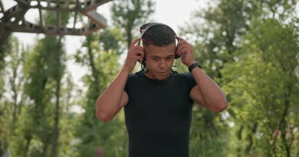 年轻而健美的非洲裔美国人 带着耳机散步 在公园里慢跑后喜欢听音乐 2X慢动作 — 图库视频影像