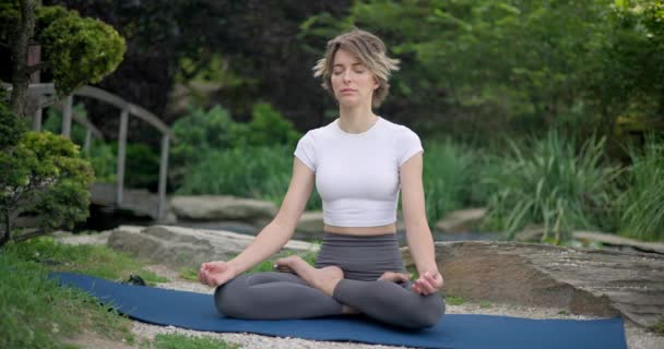 身穿运动服的年轻的高加索女人坐在户外瑜伽垫上做呼吸练习和冥想 — 图库视频影像
