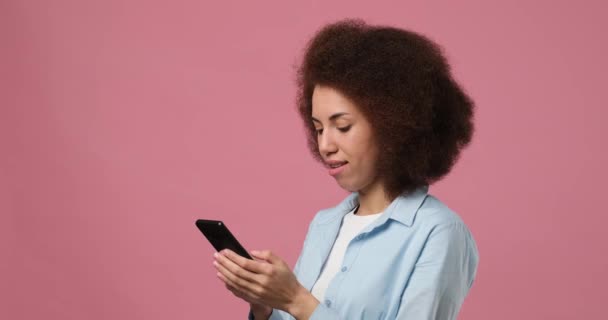 若い幸せな笑顔アフリカ系アメリカ人女性ピンクのスタジオの背景に隔離された携帯電話にテキストメッセージを入力します Dci 二重スローモーション — ストック動画