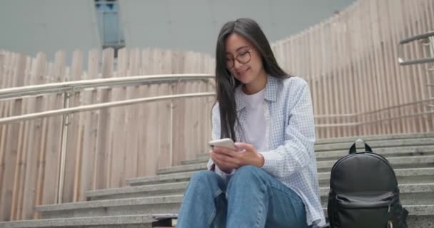 Sorrindo Asiático Jovem Estudante Assentos Femininos Nas Escadas Usando Smartphone — Vídeo de Stock