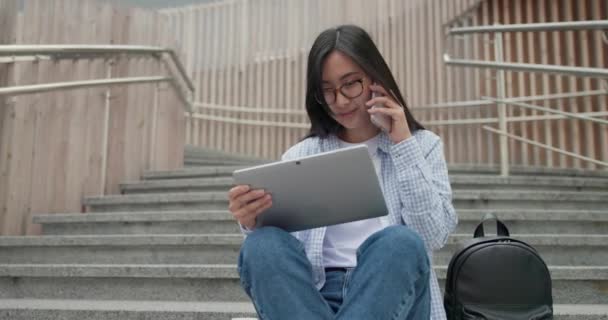 年轻的亚洲女学生坐在室外楼梯上用平板电脑垫 — 图库视频影像