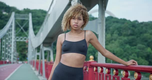 美しいアフリカ系アメリカ人女性アスリートランナー休憩疲れ切ったワイプは 都市の橋でカーディオトレーニングエクササイズ後に汗をかきます — ストック動画