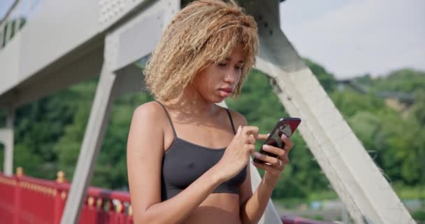 Junge Afrikanisch Amerikanische Sportlerin Mit Smartphone Freien Auf Einer Stadtbrücke — Stockvideo