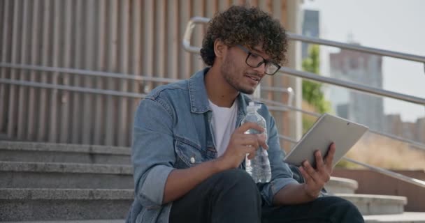 年轻英俊的印度后进男子学生自由职业者坐在户外的台阶上使用平板电脑垫 2X慢动作 — 图库视频影像