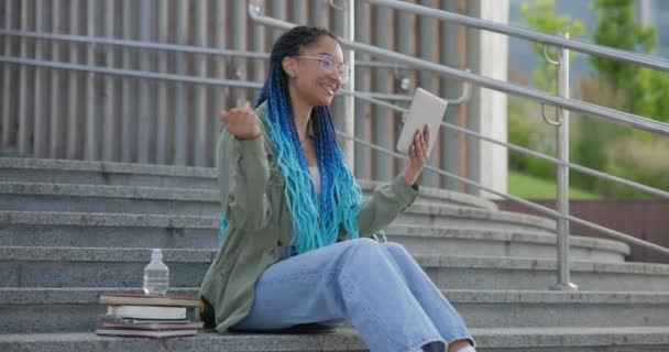 若いアフリカ系アメリカ人女性学生やフリーランサー 屋外に座っているタブレットPcパッドコンピュータを使用してビデオ通話をする — ストック動画