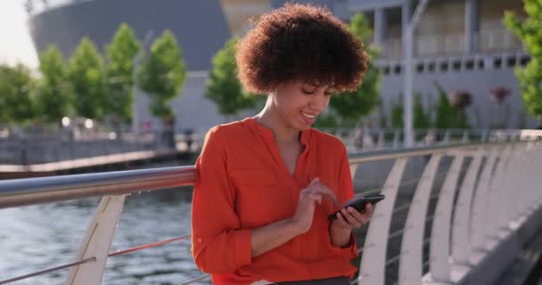 在现代城市 头发卷曲的年轻非洲裔美国妇女在户外散步时 用手机进行网上购物 约会或社交媒体 — 图库视频影像