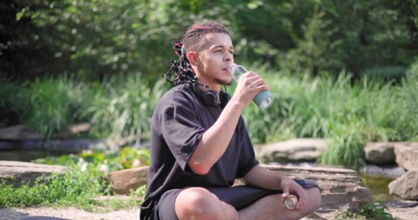 若いアフリカ系アメリカ人のスピリチュアリティマンは 公園の屋外や飲料水に座ってヨガアサナを瞑想 — ストック動画