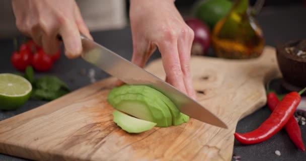 女性は 国内キッチンで木製の板にナイフで新鮮な緑色のアボカドフルーツを切断します Dciについて — ストック動画