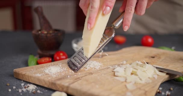 女性は 伝統的なイタリアのパルメザンハードチーズのピースを国内のキッチンで木製の切断ボードに格子を与えています Dciについて — ストック動画