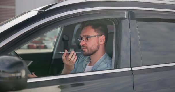 若い白人男性は駐車場の車に座り 電話で音声メモやメッセージを録音しています Dciについて — ストック動画