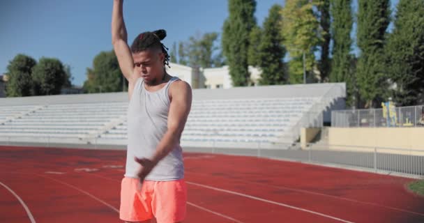 スポーツウェアの若いアフリカ系アメリカ人男性は スタジアムで心臓のトレーニングと暖かい気まぐれを作っています スローモーション — ストック動画