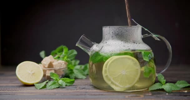 将天然的有机草本茶与柠檬和薄荷混合在玻璃杯茶壶中 配上木勺 — 图库视频影像