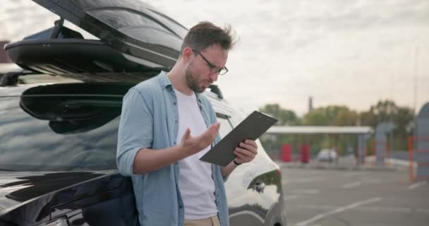 一个悲伤而愤怒的人站在一辆汽车旁边 看着发给他的账单或支票 Dci — 图库视频影像