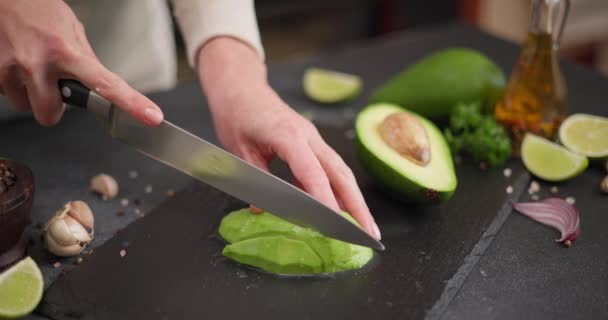ナイフでテーブルにサービングボード上の石の上に新鮮な緑のアボカドフルーツをスライスした女性 Dciについて — ストック動画