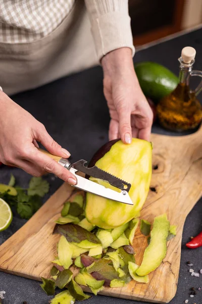 Cooking mango salsa - woman peeling mango fruit.