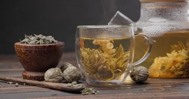 盛开的花茶球在木制背景的热开水玻璃杯茶壶中酿造 — 图库视频影像