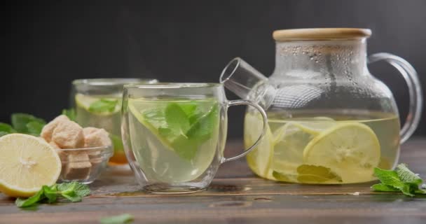 天然的有机草本茶 柠檬和薄荷放在木制桌子上的玻璃杯茶壶中 — 图库视频影像