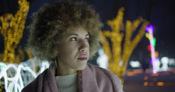 冬天的夜晚 美丽的非洲裔美国女人站在室外 背靠着花环和灯光 — 图库视频影像