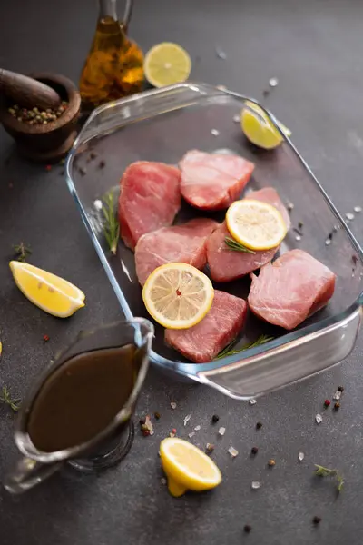 Pieces of Fresh tuna Fish fillet in glass cooking dish and soy sauce marinade in a gravy boat.