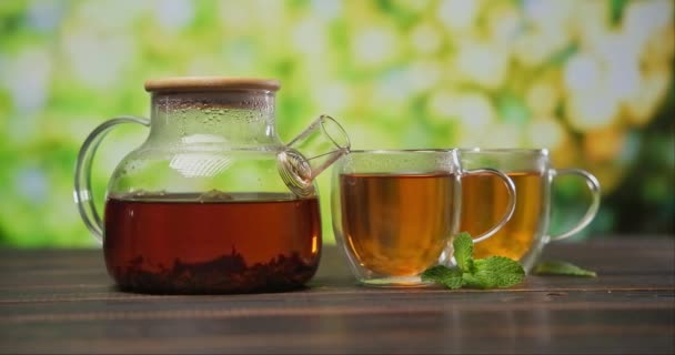 在木制桌子上的玻璃杯茶壶中酿制的有机天然茶 — 图库视频影像