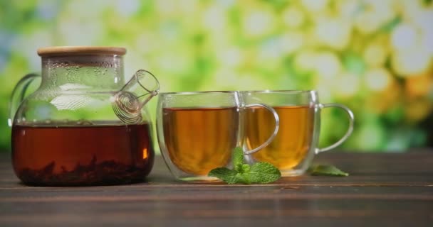 在木制桌子上的玻璃杯茶壶中酿制的有机天然茶 — 图库视频影像