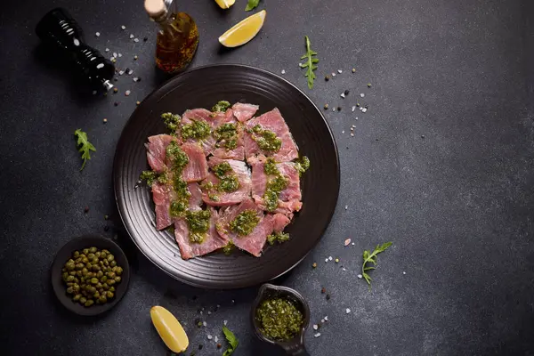 tuna carpaccio - slices of fresh raw tuna fillet on black ceramic plate.