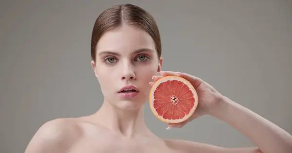 stock image Beauty, health, cosmetics, anti-aging therapy and skin care concept - young beautiful brunette Caucasian woman holding half a grapefruit in her hands, concept of vitamins, freshness, fruit power. High