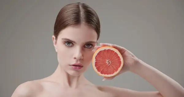 stock image Beauty, health, cosmetics, anti-aging therapy and skin care concept - young beautiful brunette Caucasian woman holding half a grapefruit in her hands, concept of vitamins, freshness, fruit power. High