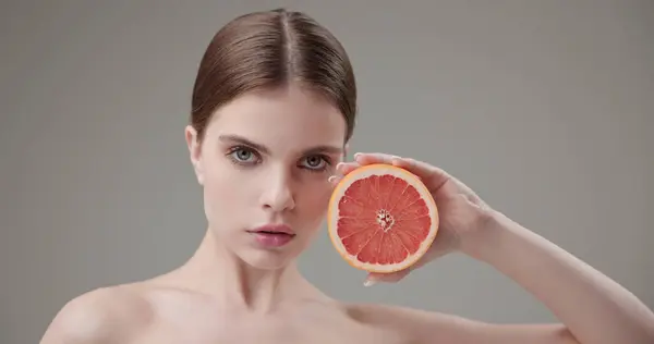 Stock image Beauty, health, cosmetics, anti-aging therapy and skin care concept - young beautiful brunette Caucasian woman holding half a grapefruit in her hands, concept of vitamins, freshness, fruit power. High