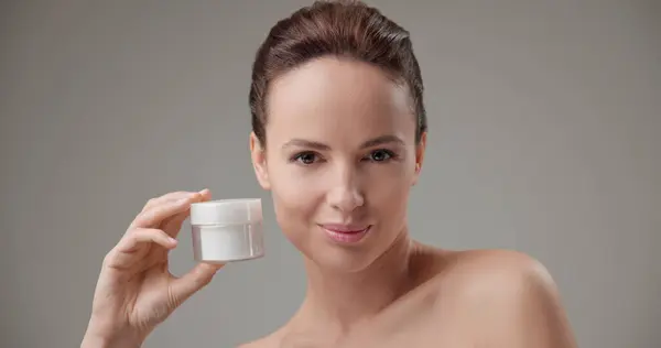 stock image Beauty, health, cosmetics, anti-aging therapy and skin care concept - young beautiful brunette Caucasian woman holding a jar of moisturizer in her hands and looking at the camera. High quality photo