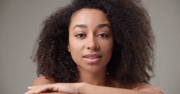 stock image Beauty and healthcare - beautiful African American woman with curly afro hairstyle and clean, healthy skin touching her face, neck, shoulders, looking at the camera with a calm look and a slight smile