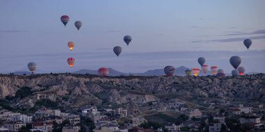 GOREME / TURKEY - 29 Haziran 2022: Şafakta gökyüzünde sıcak hava balonları ile manzara