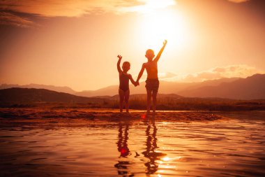 Çocuklar gün batımında denizde eğleniyor.