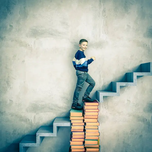 小男孩爬上一堆五颜六色的书 形状像楼梯 象征着教育和成就 免版税图库照片