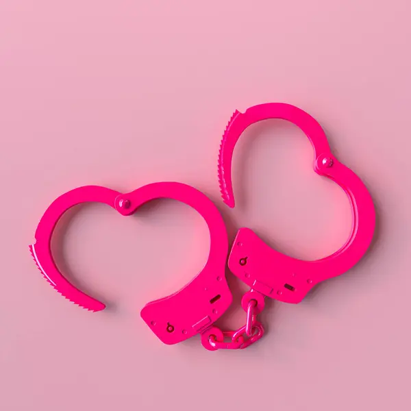 明るいピンクの手錠のペアは柔らかいピンクの背景に心臓の形を形成する ストック写真