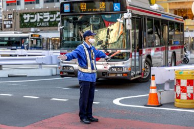 Tokyo 'da yüz maskesi takan Japon güvenlik görevlisi trafiği yönetiyor.