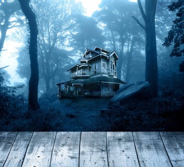 Cadılar Bayramı pankartı, perili ev ve boş tahta masa üstü. Ahşap teras döşemesi ve gece ormanında terk edilmiş bir ev. Gizemli ormanlık alandaki korkunç koloni kulübesi. Fotoğraf mavi tonda.