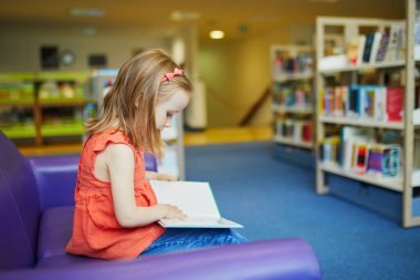 Şehir kütüphanesinde kitap okuyan 4 yaşındaki kız çocuğu.