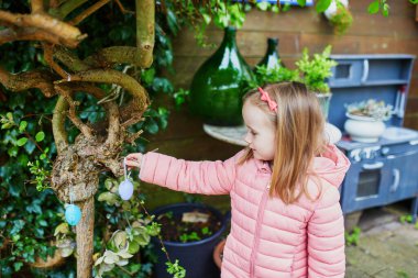 Adorable preschooler girl looking for Easter eggs hidden in the garden for the Easter tradition of egg hunt. Fun Easter activities for kids