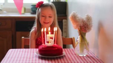 Happy little girl celebrating her fifth birthday and making a wish. Little kid with birthday cake and candle