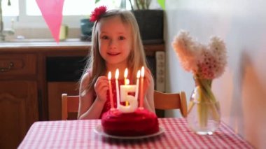 Küçük mutlu kız beşinci yaş gününü kutluyor ve bir dilek tutuyor. Doğum günü pastası ve mumu olan küçük çocuk.