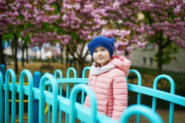 Happy 4 years old girl playing on a playground in Paris, France. Adorable preschooler girl having fun outdoors on a nice spring day under cherry blossom trees. Outdoor spring activities for kids