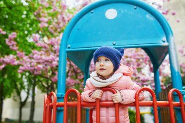 Happy 4 years old girl playing on a playground in Paris, France. Adorable preschooler girl having fun outdoors on a nice spring day under cherry blossom trees. Outdoor spring activities for kids