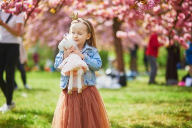 Adorable preschooler girl in tutu skirt and princess crown enjoying nice spring day in cherry blossom garden