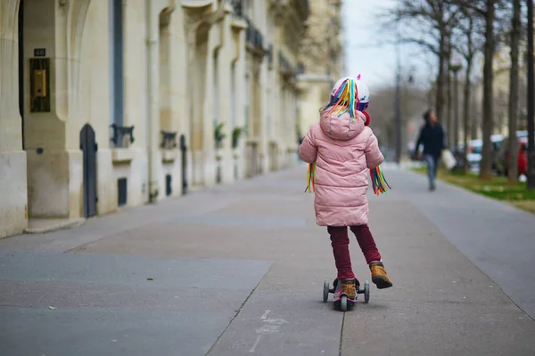 フランスの通りに彼女のスクーターに乗っている愛らしい未就学児の女の子 プッシュスクーターに乗ってユニコーンヘルメットのかわいい子供 子供のためのアクティブなレジャーや屋外スポーツ — ストック写真