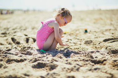 Preschooler girl playing on the sand beach at Atlantic coast of Normandy, France. Outdoor summer activities for kids
