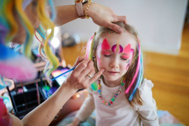 Children face painting. Artist painting little preschooler girl like unicorn on a birthday party. Creative activities for kids clipart